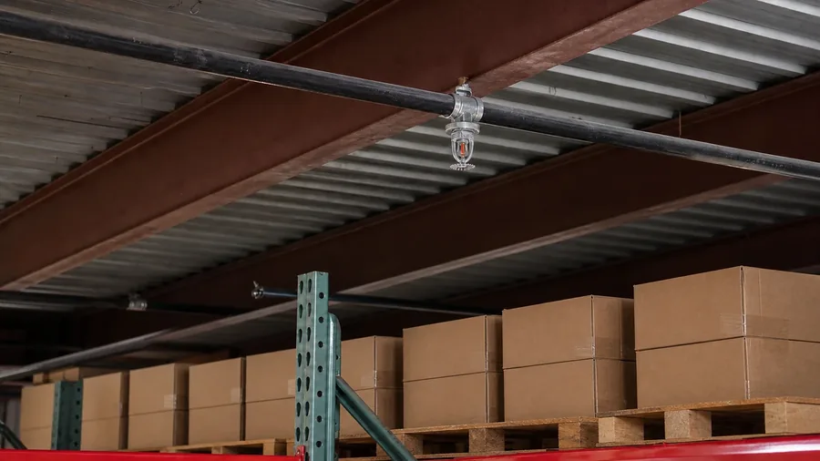 Representative AI-generated matched warehouse view with inventory reorganized lower beneath the sprinkler